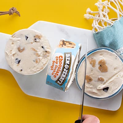 Hand holds a knife and slices a pint of Ben & Jerry's Chocolate Chip Cookie Dough ice cream into slices.