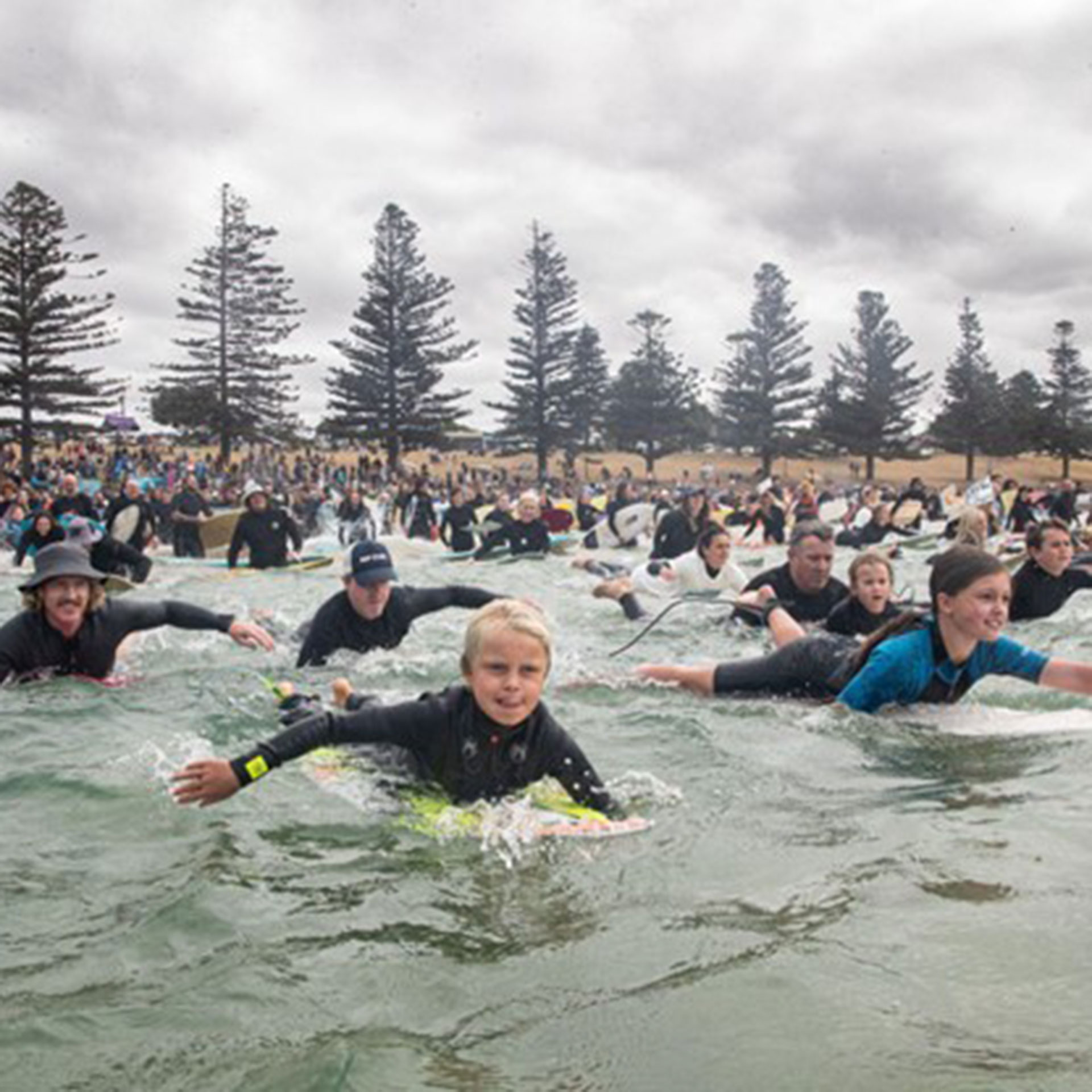 A group of many people paddling out towards the camera on surf boards