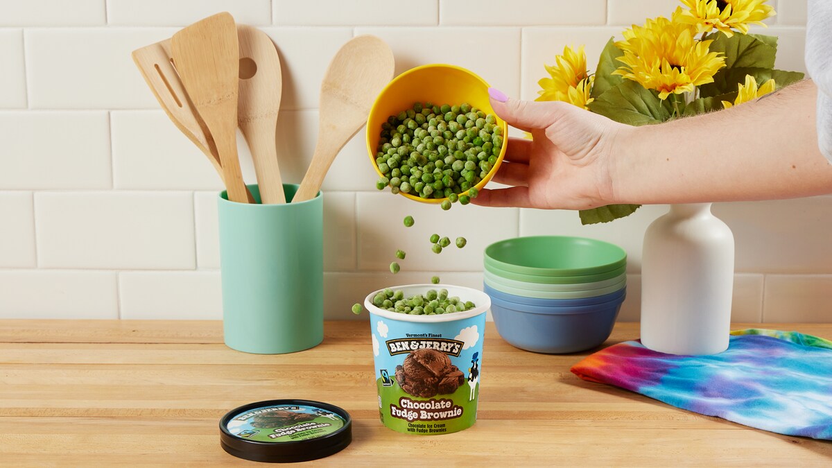 Hand dumping peas into an open pint of ice cream