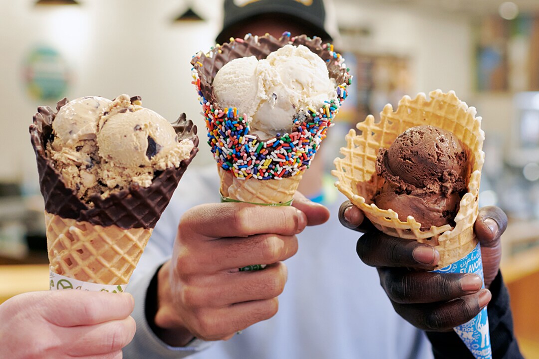 Three hands holding Ben & Jerry's freshly baked waffle cones with ice cream.