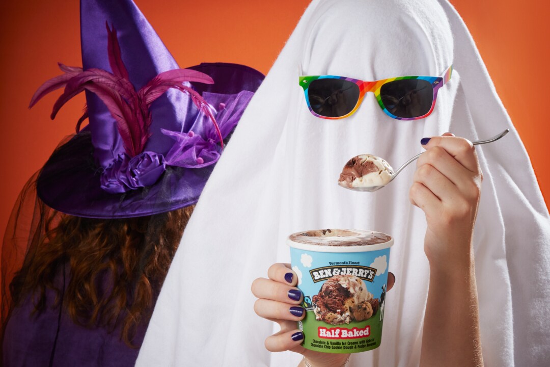 Person dressed as a ghost holds a pint of Ben & Jerry's Half Baked ice cream and scoops out a bite on a spoon.
