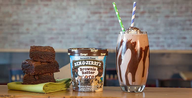 Pint of Ben & Jerry's Brownie Batter Core ice cream next to a Brownie Batter Mudslide and a stack of brownies. Kitchen setting.